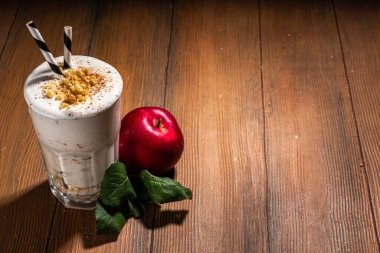 Ev yapımı elmalı turta milkshake, tart parçacıkları ve baharatlı kırmızı sonbahar elma proteini smoothie, sıcacık ahşap arka planda mevsimlik sağlıklı bir kahvaltı içeceği.