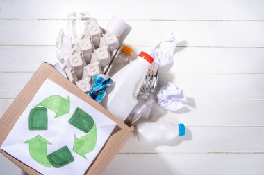 Çöp ayıklama, atık geri dönüşüm konsepti. Geri dönüşüm malzemelerinin olduğu kutu - plastik, cam, kağıt, karton, beyaz ahşap arka plan fotokopi alanı. Kadın elleri çeşitli çöp ve çöpleri ayırıyor.