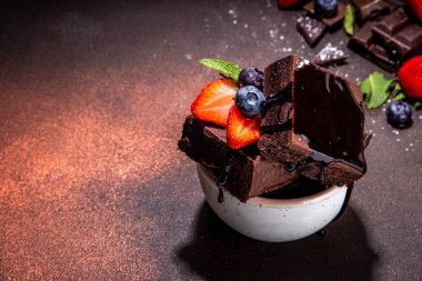 Böğürtlenli siyah çikolatalı kek. Üzerine çikolata sosu serpiştirilmiş ev yapımı kek kurabiyeleri ve koyu arkaplanda taze çilek, yabanmersini, fotokopi alanı.