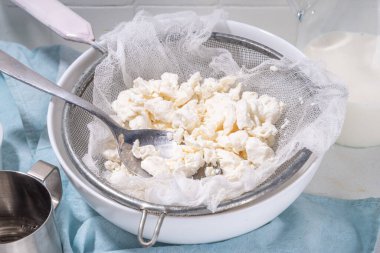 Süzme peynir yapmak, ev yapımı mayalama süt ürünü. Ev yapımı süzme peynir, mutfak masasının üzerinde kumaş poşetler, kadın elleri ev manzarası fotokopi odasında peynir emiyor.