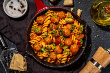 Domates soslu köfteli fusilli makarna, koyu arkaplanda otlar ve rendelenmiş peynir, üst görünüm fotokopi alanı