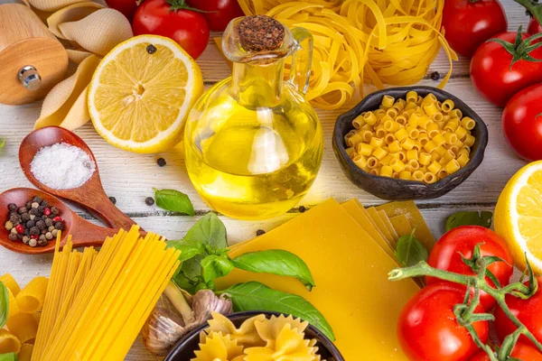Various pasta with spices and ingredients for cooking. Preparation dinner, lunch background with fresh basil, tomatoes, spices, garlic and different sort and types of italian Mediterranean pasta