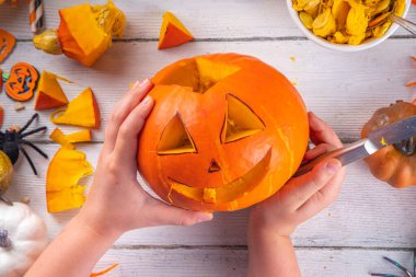 Balkabağı oyma Jack Feneri ile Cadılar Bayramı hazırlığı. Kadın, kadın ve çocuklar ellerini çerçeveye koyar, dekore eder, çizer ve korkunç Cadılar Bayramı partisini oyar.