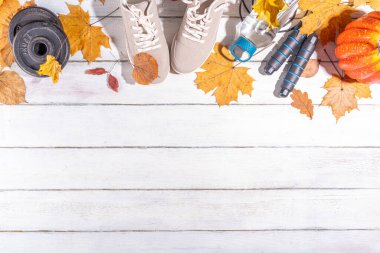 Sonbahar sporları arka planı. Açık havada sonbahar sporları konsepti. Koşan spor ayakkabılar, halter diskler, atlama halatı, su şişesi, ahşap arka plan, sonbahar yaprakları, balkabakları üst görünüm kopya alanı
