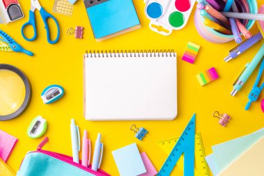 Okul ekipmanları parlak sarı düz yerde yatıyordu. Çeşitli okul ve ofis malzemeleri, aksesuarlar. Okul satışına geri dön. Üst görünüm kopyalama alanı