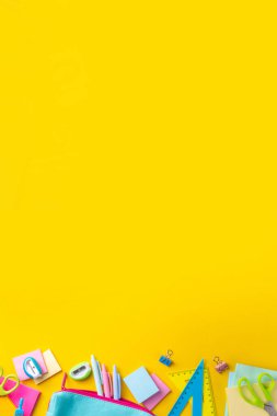 Okul ekipmanları parlak sarı düz yerde yatıyordu. Çeşitli okul ve ofis malzemeleri, aksesuarlar. Okul satışına geri dön. Üst görünüm kopyalama alanı