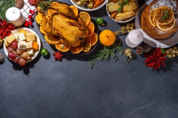 Christmas or New Year dinner foods on dark table. Set of traditional Xmas party dishes - pannetone, baked chicken, vegetables, potato, cheese and fruits plate, top view copy space