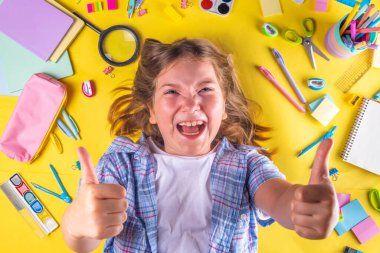 Sevimli duygusal kız okula dönmeye hazır çeşitli okul malzemeleriyle, parlak sarı arka planda eğitim aksesuarlarıyla.