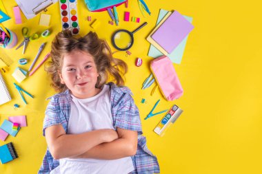 Sevimli duygusal kız okula dönmeye hazır çeşitli okul malzemeleriyle, parlak sarı arka planda eğitim aksesuarlarıyla.