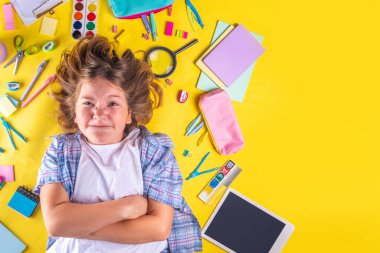 Sevimli duygusal kız okula dönmeye hazır çeşitli okul malzemeleriyle, parlak sarı arka planda eğitim aksesuarlarıyla.