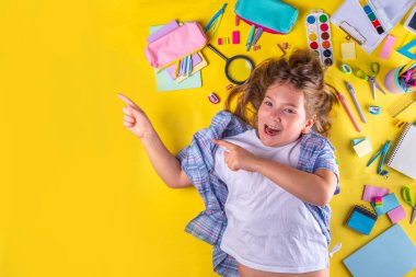 Sevimli duygusal kız okula dönmeye hazır çeşitli okul malzemeleriyle, parlak sarı arka planda eğitim aksesuarlarıyla.