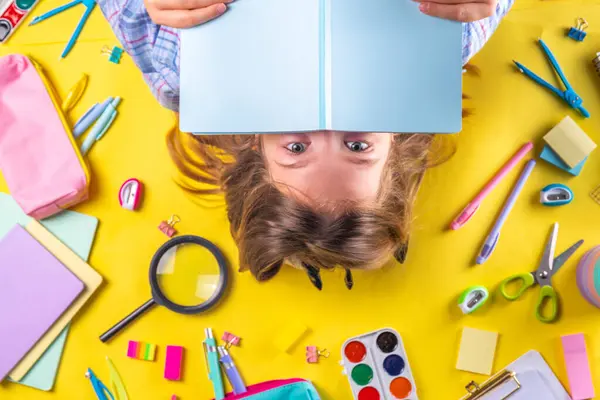 Sevimli duygusal kız okula dönmeye hazır çeşitli okul malzemeleriyle, parlak sarı arka planda eğitim aksesuarlarıyla.