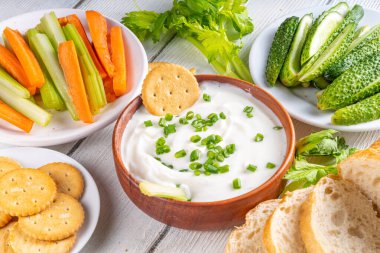 Süzme peynir yüksek proteinli sos taze sebzeler, ekmek ve krakerler ahşap masa üzerinde fotokopi alanı. Çeşitli abur cuburlarla birlikte sağlıklı peynirli diyet yemek