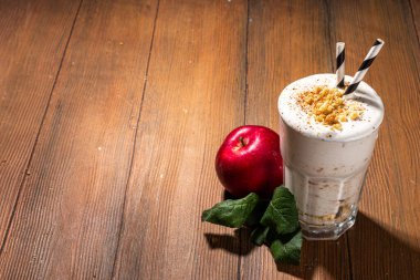 Ev yapımı elmalı turta milkshake, tart parçacıkları ve baharatlı kırmızı sonbahar elma proteini smoothie, sıcacık ahşap arka planda mevsimlik sağlıklı bir kahvaltı içeceği.