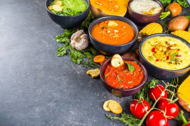 Farklı sonbahar çorbaları seti. Portakal kaselerinde çeşitli sebze çorbaları - mısır, patates, balkabağı, domates, kabak, brokoli kremalı çorba. Siyah beton arkaplanda üst görünüm kopyalama alanı