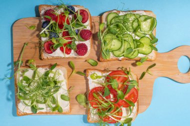 Vegetable and fruit microgreen sandwiches. Homemade toasts sandwiches with tomato, cucumber, berry fruits and a lot of microgreen baby leaves sprouts, white table background copy space