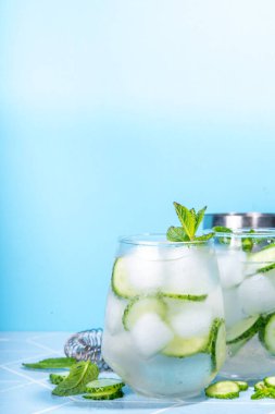 Ferahlatıcı yaz içeceği. Nane şekeri, salatalık, limon kokteyli. Açık mavi fayanslı masa, parlak güneş ışığı, kopyalama alanı. İki bardak salatalıklı su ya da limonata, sağlıklı diyet içecek.