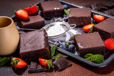 Böğürtlenli siyah çikolatalı kek. Üzerine çikolata sosu serpiştirilmiş ev yapımı kek kurabiyeleri ve koyu arkaplanda taze çilek, yabanmersini, fotokopi alanı.