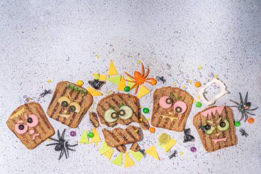 Funny halloween monster sandwiches. Set of various decorated monster sandwich and toasts, with cucumber, cheese and meat sausages, white table background with Halloween decorations