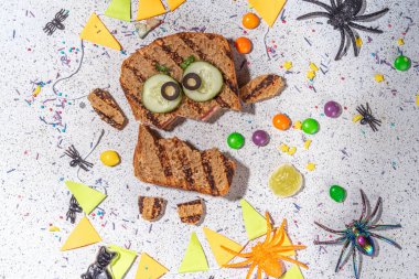 Funny halloween monster sandwiches. Set of various decorated monster sandwich and toasts, with cucumber, cheese and meat sausages, white table background with Halloween decorations