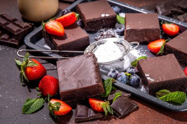 Böğürtlenli siyah çikolatalı kek. Üzerine çikolata sosu serpiştirilmiş ev yapımı kek kurabiyeleri ve koyu arkaplanda taze çilek, yabanmersini, fotokopi alanı.