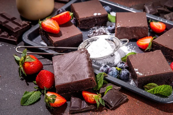 Böğürtlenli siyah çikolatalı kek. Üzerine çikolata sosu serpiştirilmiş ev yapımı kek kurabiyeleri ve koyu arkaplanda taze çilek, yabanmersini, fotokopi alanı.