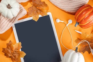 Tablet, kulaklık, beyaz, turuncu balkabağı ve turuncu arka planda sonbahar yaprakları olan samimi bir sonbahar arkaplanı. Sonbahar durgun yaşam kompozisyonu. 