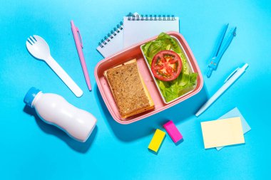 Healthy school meal, back to school concept. Children packed lunch box with balanced diet snack food - yogurt, cereal toast sandwich, apple, fresh vegetable salad, high-colored bright background