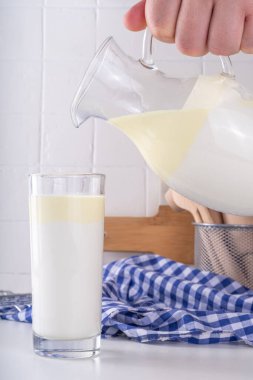 Homojen olmayan, tam yağlı süt, kremalı süt ürünü, kremalı süt konsepti. Doğal organik çiftlik, cam ve sürahide pastörize edilmemiş süt, beyaz mutfak masasında fotokopi alanı.