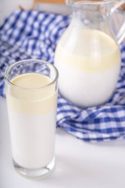 Homojen olmayan, tam yağlı süt, kremalı süt ürünü, kremalı süt konsepti. Doğal organik çiftlik, cam ve sürahide pastörize edilmemiş süt, beyaz mutfak masasında fotokopi alanı.