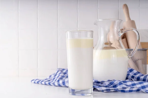 Non-Homogenized, whole milk, cream-top layered dairy product, Creamline Milk concept. Organic farm natural, unpasteurized milk in glass and jug, on white kitchen table copy space
