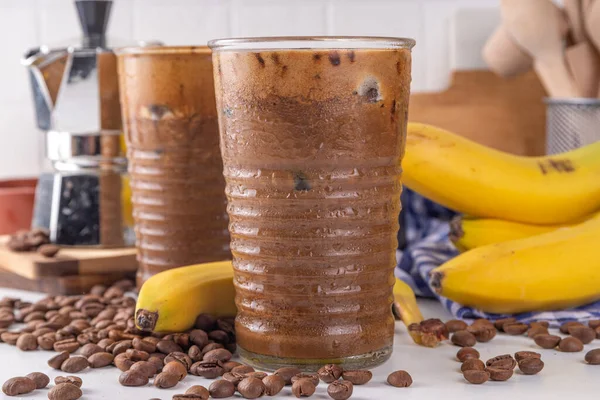Blended banana coffee. Cold latte coffee and banana non-dairy, vegan diet drink with frozen bananas and espresso, on white kitchen table copy space