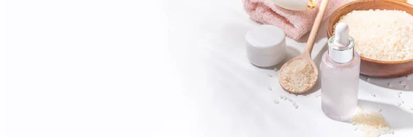 セラム 天然有機米の化粧品 発酵した美容ケア ウェルネス 透明な白い血清は白い浴室の背景の米の穀物および浴室の道具が付いているびんを落とします — ストック写真