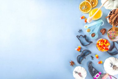 Cadılar Bayramı zencefilli kurabiye pişirme arka planı. Sonbahar tatili pişirme konsepti, malzemeler, baharatlar, cadılar bayramı sembolü kurabiye kesiciler - balkabağı, hayalet, yarasa, cadı şapkası, üst görünüm mavi masa fotokopisi alanı