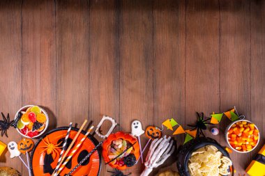 Cadılar Bayramı tatlıları ve abur cubur masası. Cadılar Bayramı partisi yemekleri, şekerler, abur cuburlar, tatil kostümleri, balkabağı kovaları, ahşap arka plan fotokopi alanı.