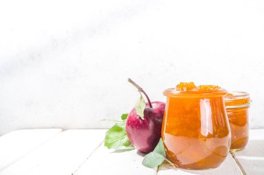 Ev yapımı altın sarısı elma reçeli, çiftlik kırmızı elmaları ve beyaz ahşap arka planda yapraklar kopyalama alanı