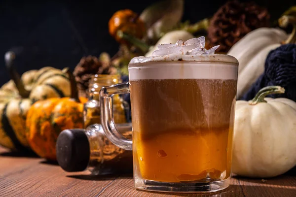 Glass cup with tasty pumpkin spice latte, with white and orange pumpkin squash, pumpkin pie spices and autumn decor copy space. Traditiional autumn Thanksgiving holiday drink
