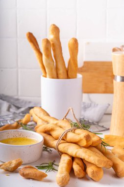 İtalyan Akdeniz Grissini ekmek çubukları, beyaz mutfak arka planında aromatik yağ ve biberiye filizleri ile