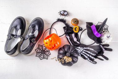 Çocukların Cadılar Bayramı partisi için hazırlıklar, şeker mi şaka mı geleneği. Geleneksel çocuk Cadılar Bayramı kostümlü cadı, hayalet, iskelet, balkabağı aksesuarları, şeker kovası, beyaz arka planda dekor.