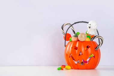 Kadın ya da çocuk elleri, içi şeker dolu bir balkabağı kovasını tutuyor. Çocuklar için Cadılar Bayramı şaka mı şeker mi partisi geçmişi, şaka mı şeker mi eğlenmek, cadılar bayramı davetiyesi, indirim veya tebrik kartı