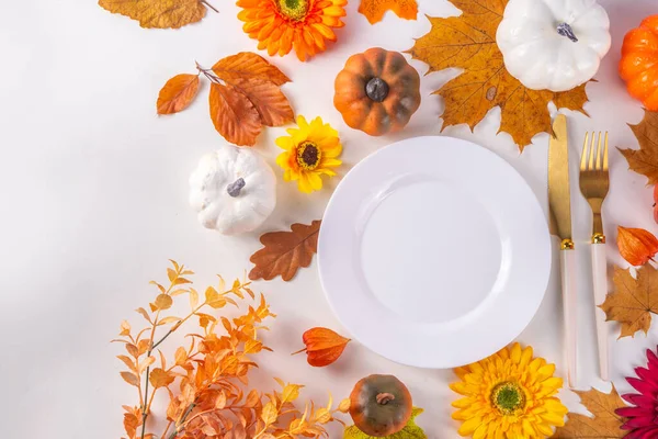 Autumn holiday table setting. Thanksgiving holiday menu, greeting card. White kitchen table with plate and cutlery, fall leaves, flowers and decor flat lay top view copy space