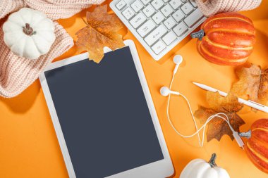 Tablet, kulaklık, beyaz, turuncu balkabağı ve turuncu arka planda sonbahar yaprakları olan samimi bir sonbahar arkaplanı. Sonbahar durgun yaşam kompozisyonu. 