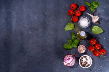 İtalyan yemekleri pişirmek için kullanışlı bir arka plan - domates, fesleğen yaprağı, yeşiller, zeytin yağı, tuz, biber, sarımsak, düz siyah beton masa üstü görünüm alanı 