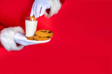 Noel Baba 'nın eli, geleneksel Noel kurabiyesi atıştırmalığıyla süt bardağıyla. Noel Baba Batıran Kurabiye, parlak kırmızı yırtık kağıt delikli arka planda. Mutlu Noeller ve mutlu yıllar tebrik kartı.