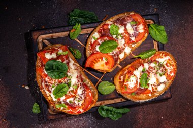 Hot loaded pizza sandwiches with tomatoes, mozzarella cheese and pepperoni, on dark background with herbs, olive oil and spices