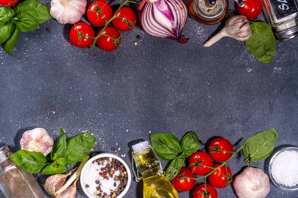 Black cooking background with useful cooking italian Mediterranean ingredients - tomatoes, basil leaves, greens, olive oil, salt, pepper, garlic, flat lay black concrete table top view copy space