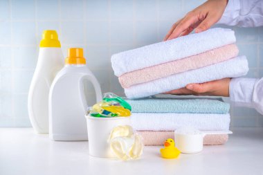 Çamaşır, çamaşır ve temizlik konsepti. Bir yığın temiz havlu, çeşitli deterjanlar - jeller, kapsüller, toz, çamaşır sepeti ve sevimli sarı ördek, beyaz banyo arka plan fotokopisi