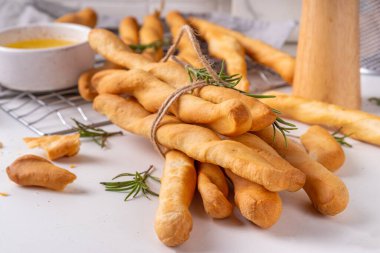 İtalyan Akdeniz Grissini ekmek çubukları, beyaz mutfak arka planında aromatik yağ ve biberiye filizleri ile