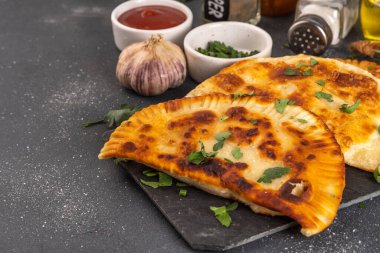 Chebureks, empanadas. Fried pies pasties, with meat and spices, on a black concrete background with herbs and tomato sauce clipart