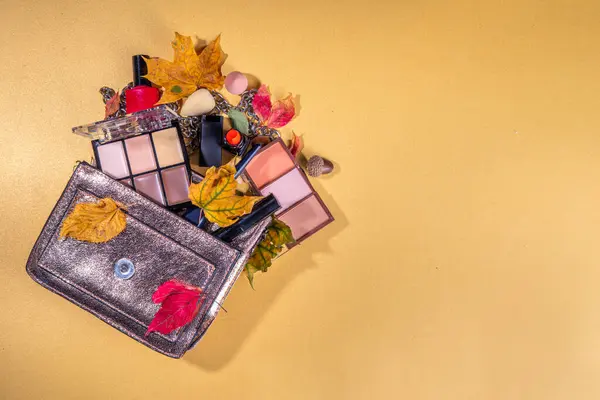 Autumn make up set on golden table background, with autumn leaves and beauty accessories. Various makeup professional cosmetics - shadows, lipstick, corrector, mascara, eyeliner, bronzer, blush